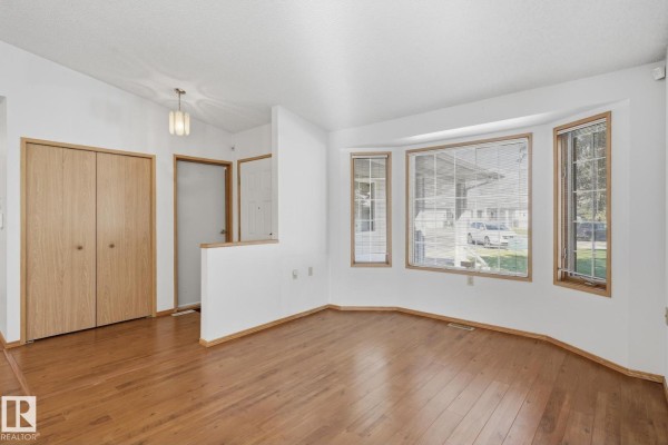 Living room showing hardwood floors, white walls, a closet, and a prominent bay window. - 7527 138a Av Nw, Edmonton