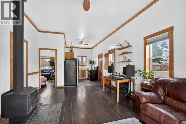 Living room with dark wood floors, a wood stove, a large television, and a sliding glass door. - 754 Wood Road, Kelowna