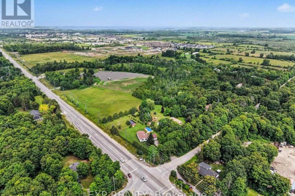 Aerial view of 7540 Highway 15 Highway E, Beckwith, at a highway intersection surrounded by trees and homes. - 7540 Highway 15 Highway E, Beckwith