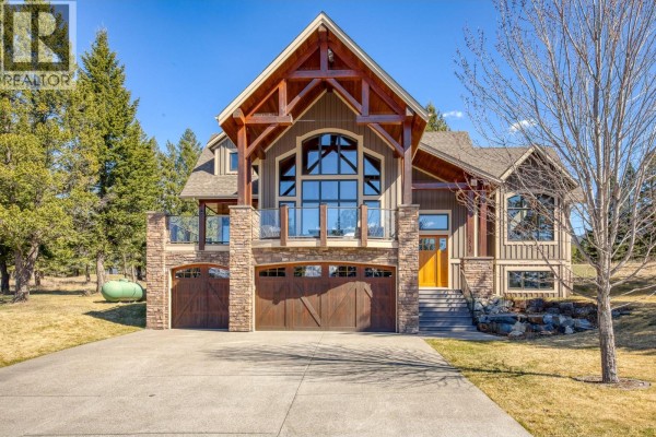Rear view of a large, two-story mountain home with a covered porch and fire pit area at sunset. - 7540 Springs Terrace, Radium Hot Springs