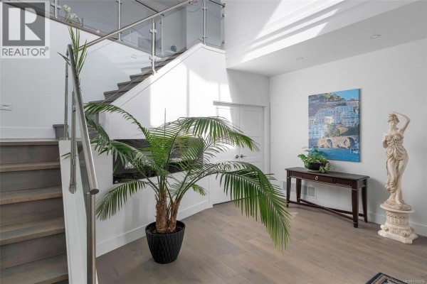 Interior view of a bright white entryway with a staircase, glass railing, and large potted plant. - 755 Butterfield Rd, Mill Bay