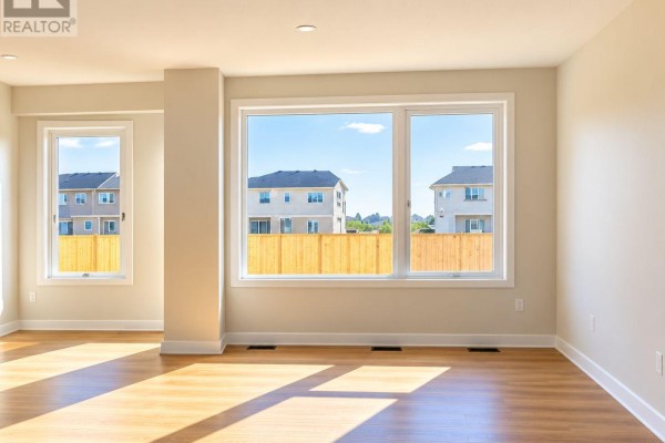 Living room with light wood floors, large windows, and a view of nearby townhouses. - 755 Haflinger Row, Ottawa