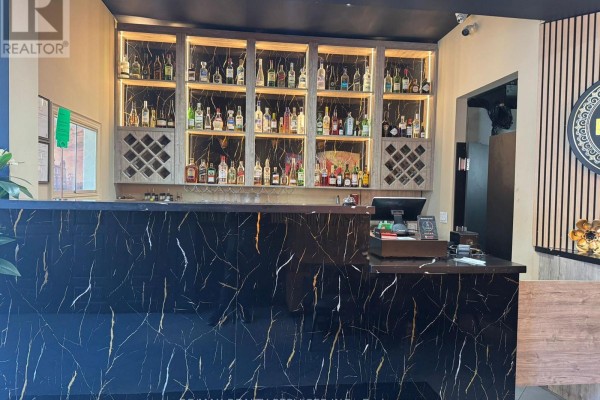 Black marble counter with gold veining and a lit wooden shelf displaying bottles behind it. - 755 Queen Street E, Toronto