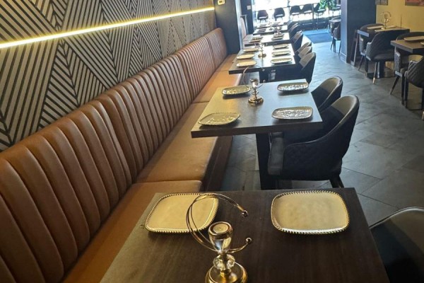 Restaurant seating with a long brown leather banquette, dark wood tables, and chairs with patterned backs. - 755 Queen Street E, Toronto