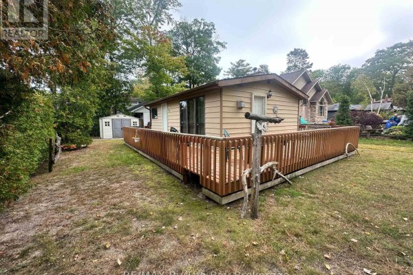 View of the cottage exterior with a large wooden deck and surrounding trees. - 755 Shore Lane, Wasaga Beach