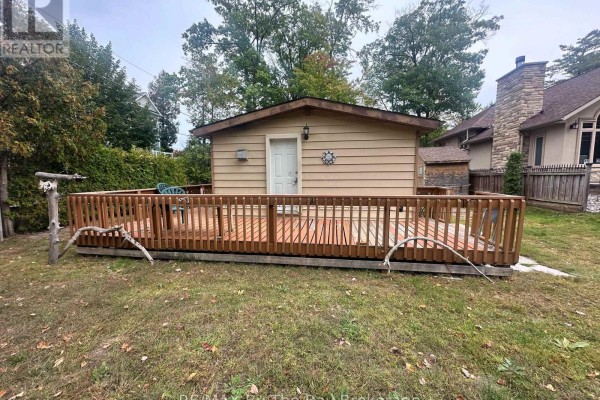 Rear view of the cottage exterior showing a wooden deck and a back door. - 755 Shore Lane, Wasaga Beach