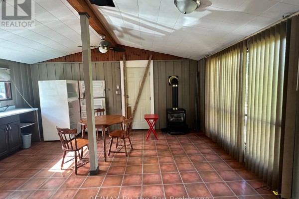 Interior room with terracotta tile floor, wooden table, chairs, and a black wood stove. - 755 Shore Lane, Wasaga Beach