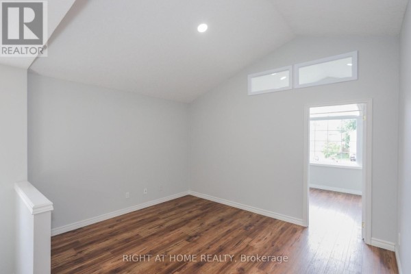 Empty room with vaulted ceiling, wood floors, and view into another room. - 756 Hedgerow Place, London North