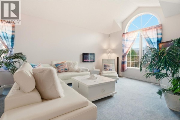Living room with a large white sectional sofa, mirrored closet doors, and an arched window. - 756 Springrose Way, Kelowna