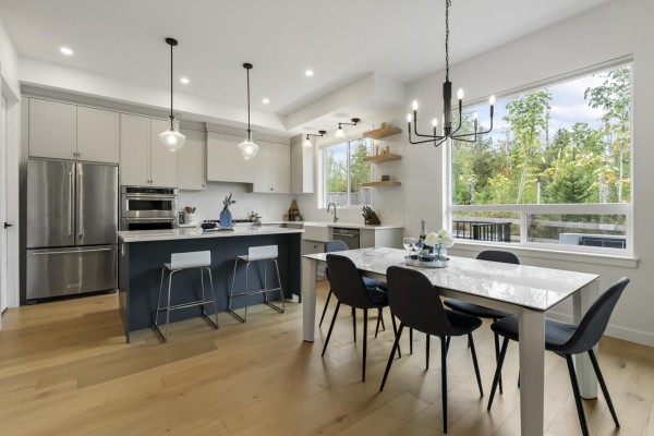Modern kitchen and dining area with stainless steel appliances, gray cabinets, and a white dining table. - 7567 196a Street, Langley