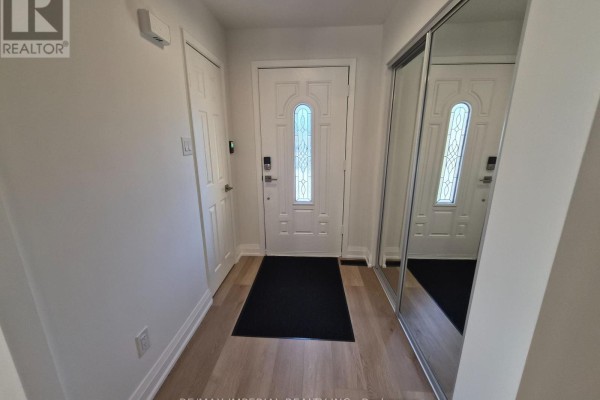 A home entryway with a white front door, mirrored closet doors, and light wood laminate flooring. - 757 Pam Crescent, Newmarket