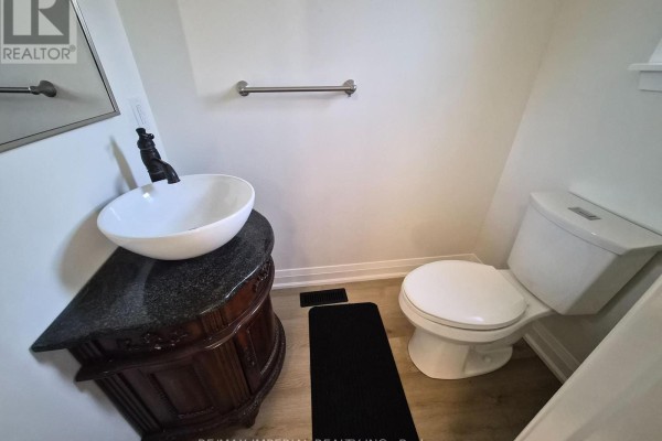 A powder room with a pedestal sink, black faucet, white toilet, and light wood laminate flooring. - 757 Pam Crescent, Newmarket