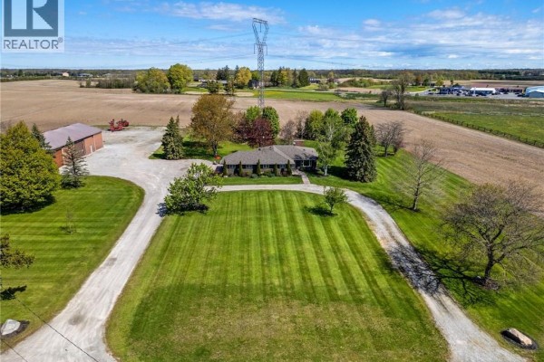 Brown barn with three large garage doors and a gravel driveway surrounded by mature trees. - 759 Concession 14 Walpole Road, Hagersville