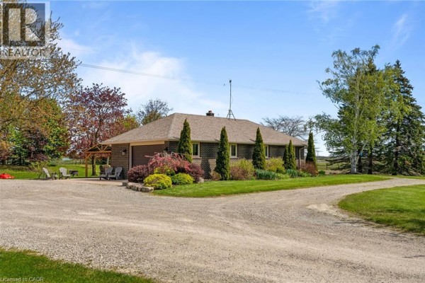 Front facade of a brick bungalow at dusk, with illuminated windows and a green lawn. - 759 Concession 14 Walpole Road, Hagersville