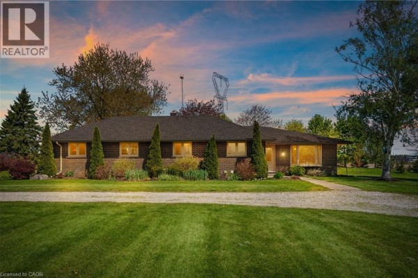 Front view of a single-story brick house with a wide lawn and mature trees. - 759 Concession 14 Walpole Road, Hagersville