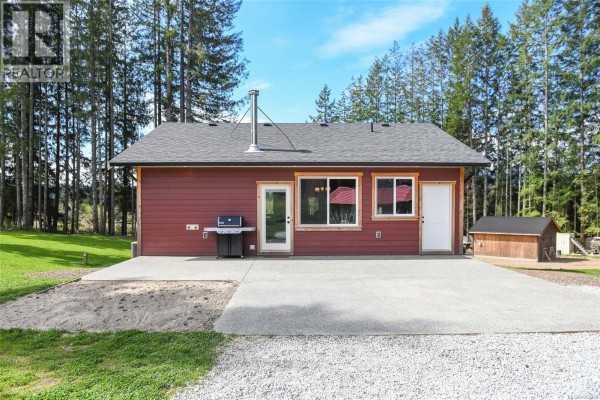 Rear view of the red house with a large garden bed and a small shed. - 7594 Island Hwy N, Merville