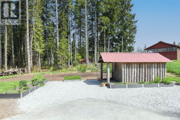 Covered wooden porch and stairs with a view of a grassy field and forest. - 7594 Island Hwy N, Merville