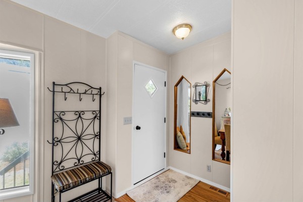 Interior entryway with a white door, coat rack, bench, and decorative mirrors, leading to the dining area. - 76 45640 Watson Road, Garrison Crossing, Chilliwack
