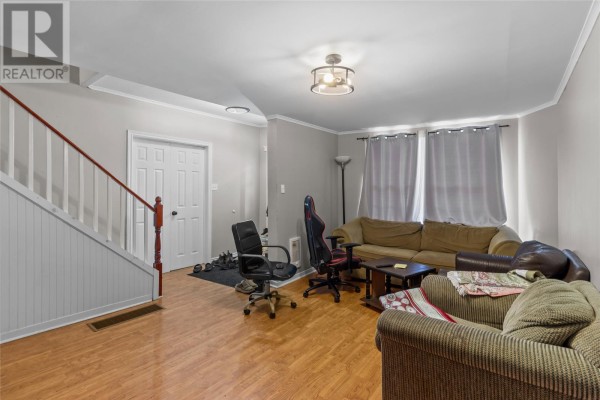 Living room furnished with a sofa, armchairs, and gaming chairs, next to a staircase. - 76-78 Goodridge Street, St  John S
