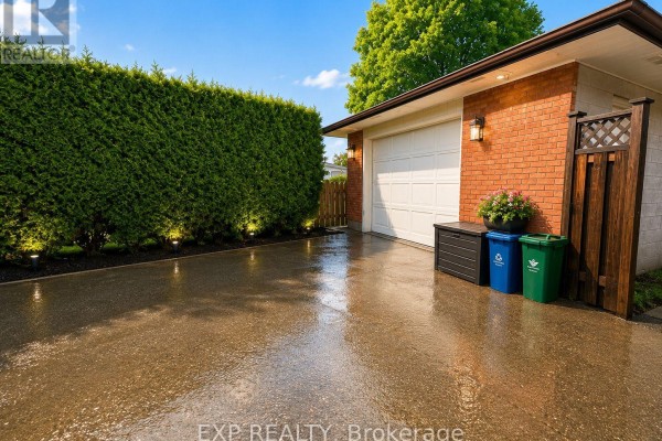 Wet asphalt driveway next to a brick garage with a white door. - 76 Appalachian Crescent, Kitchener