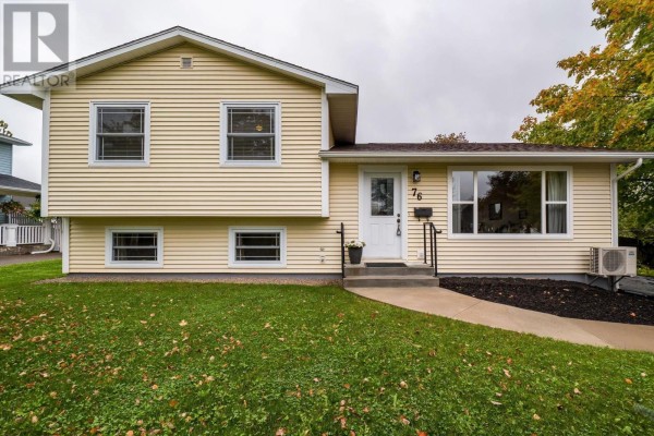 Front view of the cream-colored split-level house with a manicured green lawn and shrubs. - 76 Appletree Lane, Kentville