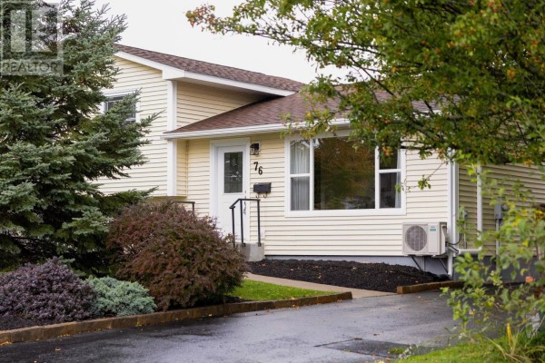 Side view of the cream-colored house exterior with pine trees and colorful shrubs in the foreground. - 76 Appletree Lane, Kentville