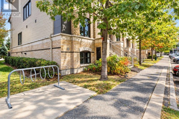 Side view of a townhouse complex with a sidewalk, grass, and bike rack. - 76 Argent Private, Ottawa