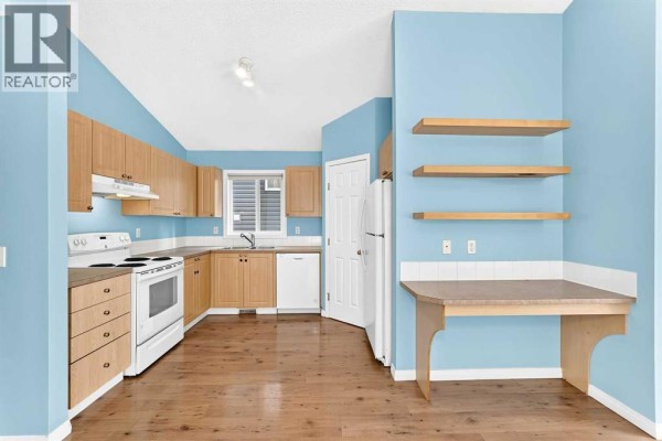 Kitchen with light blue walls, wood cabinets, white appliances, and hardwood floors. - 76 Coville Close Ne, Calgary