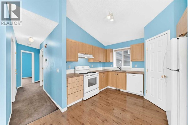 Kitchen and hallway view with light blue walls, wood cabinets, and white appliances. - 76 Coville Close Ne, Calgary