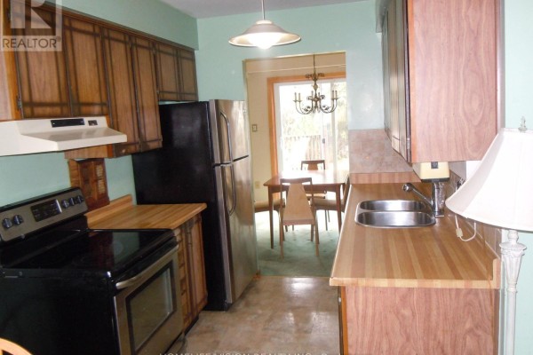 Kitchen with wood cabinets, stainless steel refrigerator, and gas stove looking into a dining area. - 76 Crayford Drive, Toronto