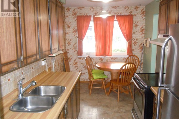 Kitchen nook with a round wooden table and chairs, floral wallpaper, and orange curtains. - 76 Crayford Drive, Toronto
