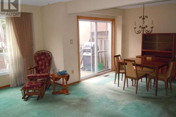 Dining area with a sliding glass door to the backyard, a wooden table, and a rocking chair. - 76 Crayford Drive, Toronto