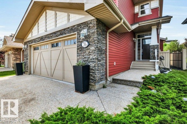 Close-up of the house exterior showing the stone pillar, red siding, garage door, and front steps. - 76 Everitt Dr N, St  Albert