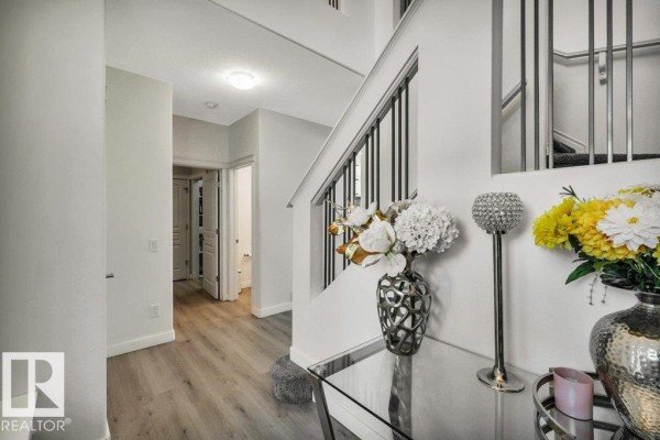 Foyer with light wood-look flooring, white walls, and a glass console table with floral arrangements. - 76 Everitt Dr N, St  Albert