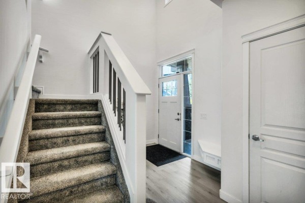 Staircase with grey carpet treads, white risers, black metal spindles, and a white front door. - 76 Everitt Dr N, St  Albert