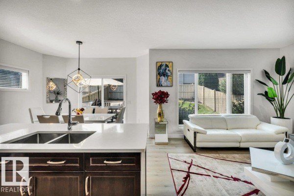 Open concept living and kitchen area with a large island, white couch, dining table, and backyard view. - 76 Everitt Dr N, St  Albert