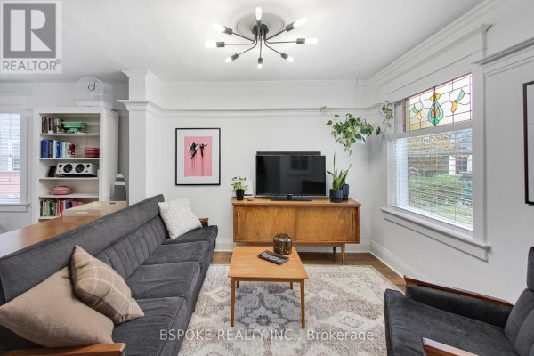 Living room with grey sofa, wooden media console, and stained glass window detail. - 76 Hiltz Avenue, Toronto