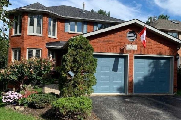 Red brick house with a two-car garage with blue doors and Canadian flag. - 76 Mayfair Drive, Barrie