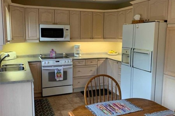Kitchen corner with light wood cabinets, white appliances, and a wooden table. - 76 Mayfair Drive, Barrie