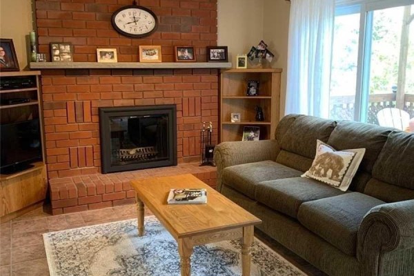Living room with a large brick fireplace, sofa, coffee table, and bookshelf. - 76 Mayfair Drive, Barrie