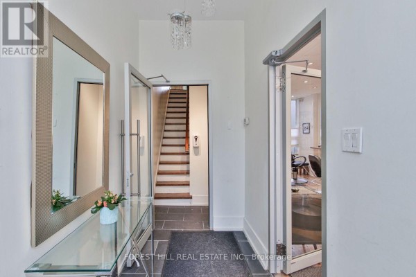 Reception area with grey tufted sofa, glass coffee table, white reception desk, and mirrored walls. - 76 Scollard Street, Toronto