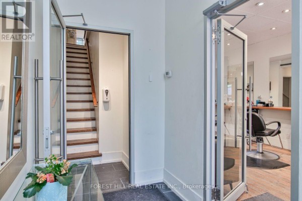 Reception area with white reception desk, sofa, glass tables, mirrors, and doorway to stairs. - 76 Scollard Street, Toronto