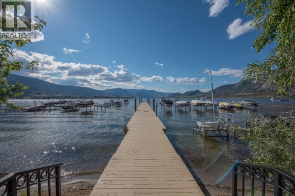 Wooden boardwalk extending into a lake with covered boat slips on either side. - 7600 Cottonwood Drive Unit# 17, Osoyoos