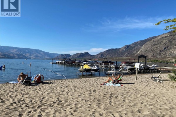Beach scene with people relaxing near docked boats and jet skis under a clear sky. - 7600 Cottonwood Drive Unit# 17, Osoyoos