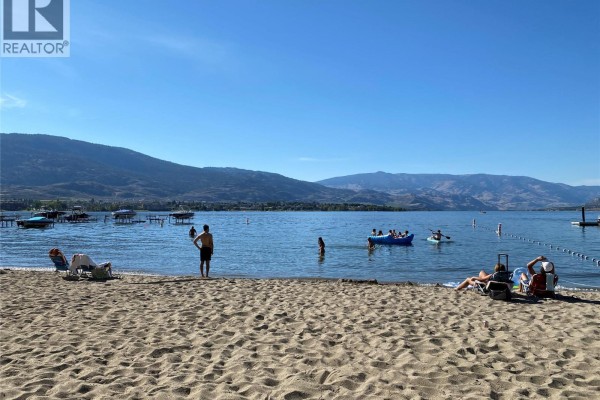 People enjoying Osoyoos lake and beach with boats docked and mountains in the distance. - 7600 Cottonwood Drive Unit# 425, Osoyoos