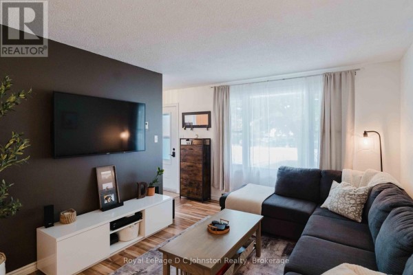 Living room with a charcoal sectional sofa, white media unit with a TV, and wood flooring. - 761 Arlington Street, Saugeen Shores