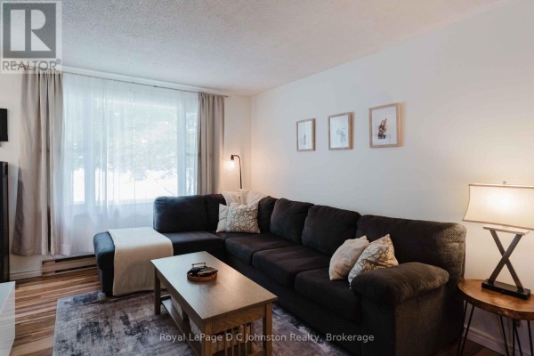 Living room featuring a charcoal sectional sofa, large window with sheer curtains, and hardwood floors. - 761 Arlington Street, Saugeen Shores
