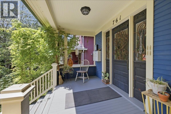 Covered porch with seating, dark blue double doors, and decorative metalwork. - 761 E 15th Avenue, Vancouver