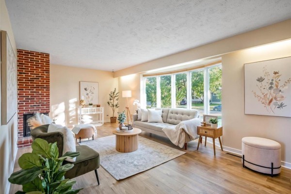 Living room with a bay window, brick fireplace, light beige walls, and wood floors. - 761 Hoskin Avenue, Winnipeg