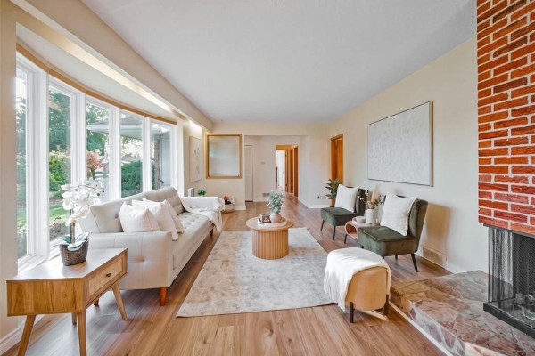Living room with bay windows, brick fireplace, and two green accent chairs. - 761 Hoskin Avenue, Winnipeg